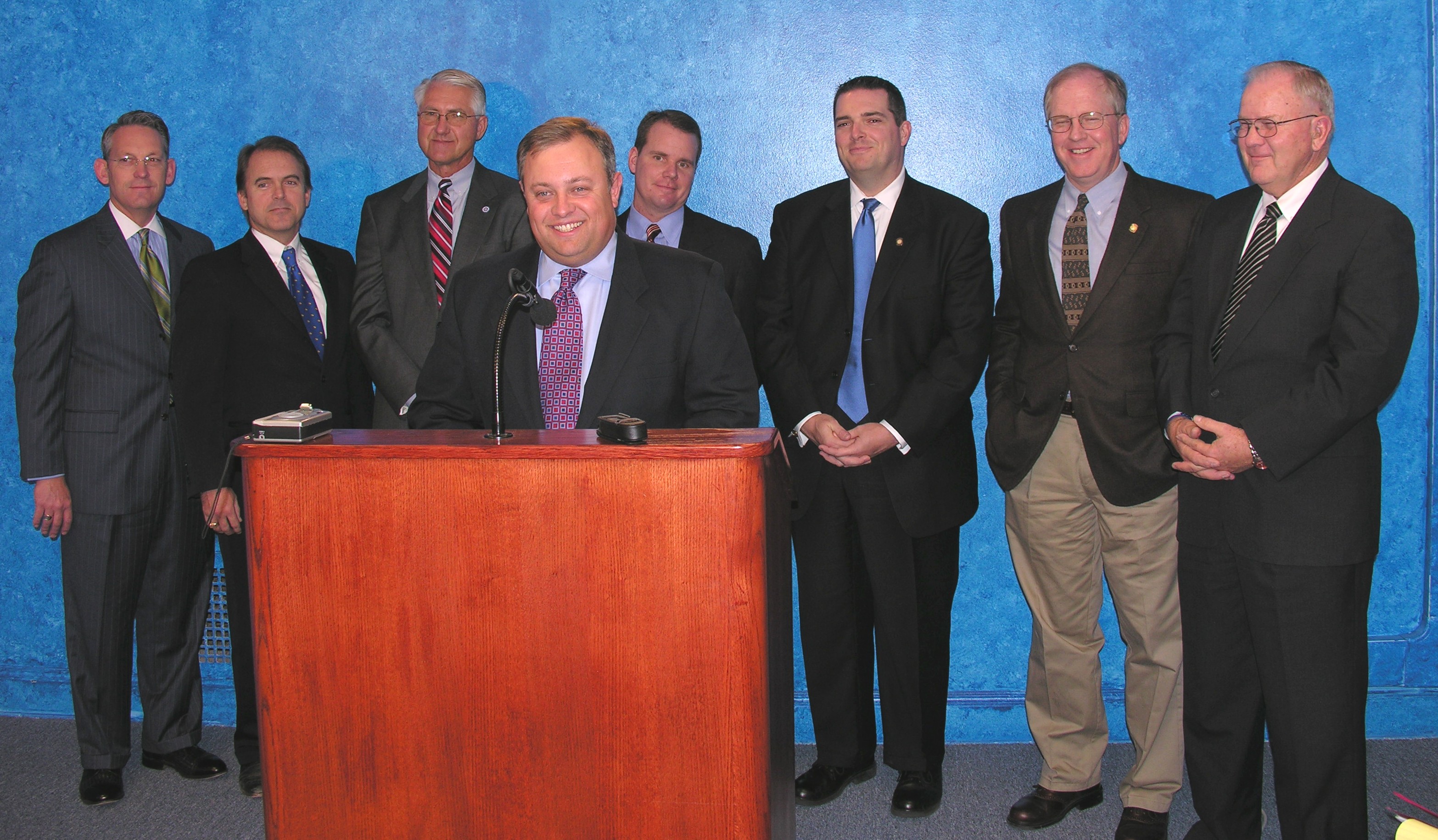 Senate Minority Leader Glenn Coffee speaks at the podium with Republican Senators Cliff Aldridge, Jonathan Nichols, Harry Coates, Todd Lamb, Clark Jolley, Owen Laughlin and David Myers.